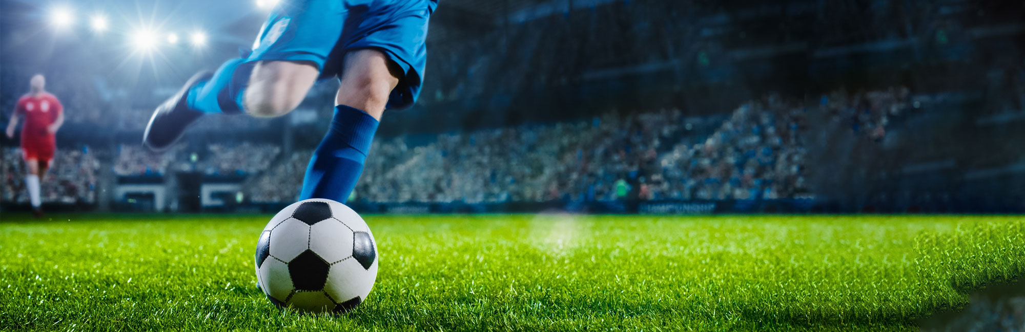 Soccer player in blue uniform preparing to kick the ball on a professional synthetic turf field under stadium lights. The high-performance artificial grass ensures durability and optimal playing conditions for competitive matches