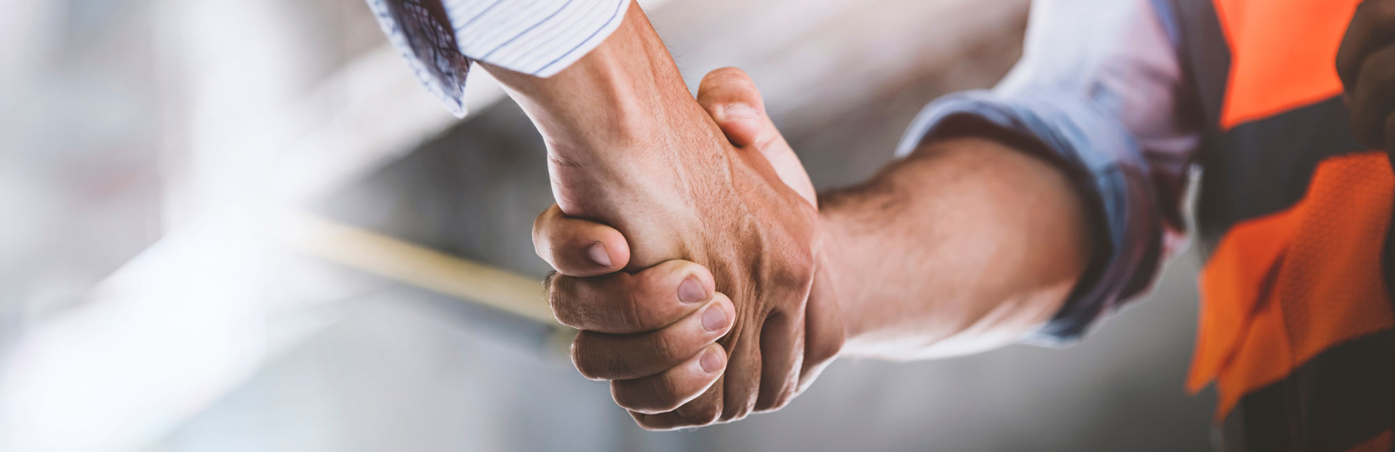 Close-up of a handshake between two professionals, one wearing an orange construction vest, symbolizing partnership and agreement.