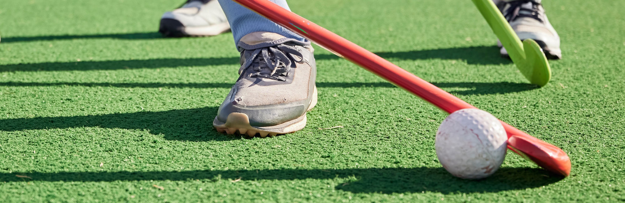 Field hockey players in action on a synthetic turf field, focusing on a ball and red hockey stick