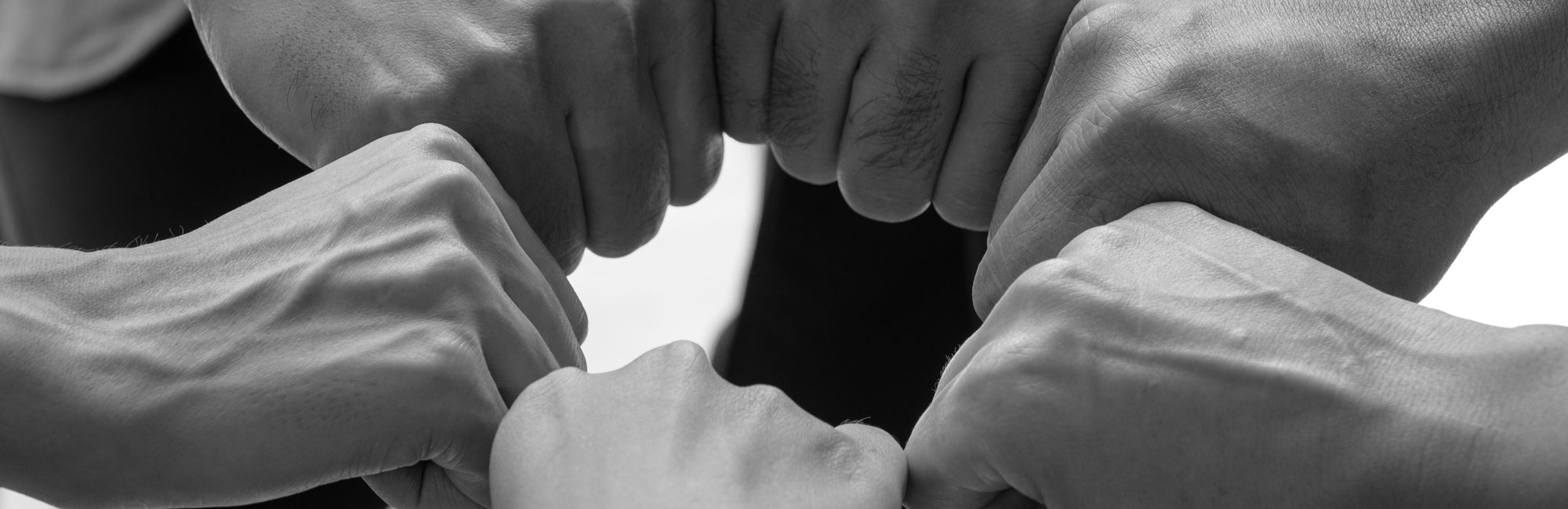 A close-up black and white image of multiple hands coming together in a fist bump, symbolizing teamwork and unity.