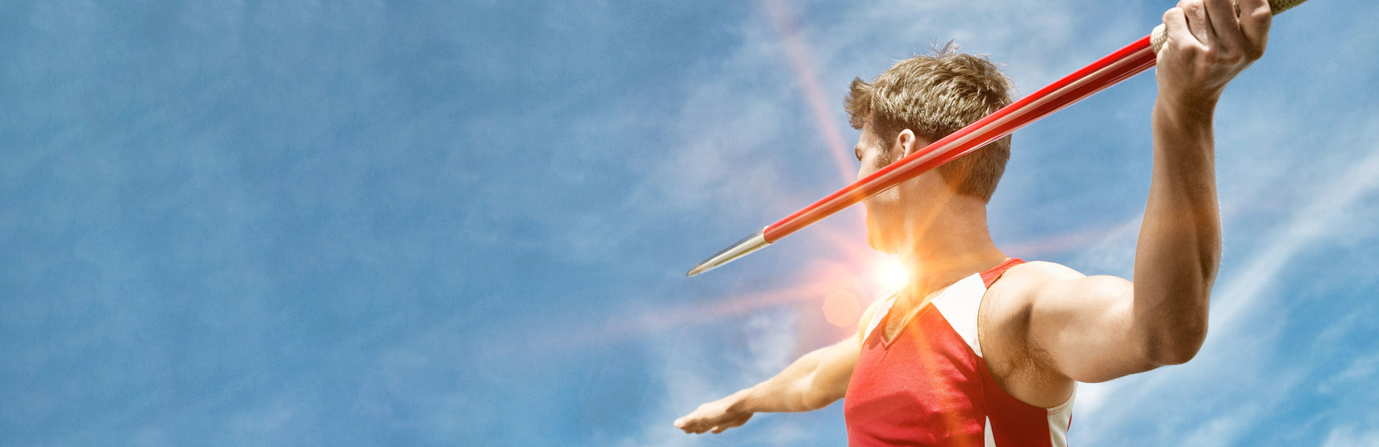 Javelin thrower in action, preparing to release the spear against a blue sky backdrop.