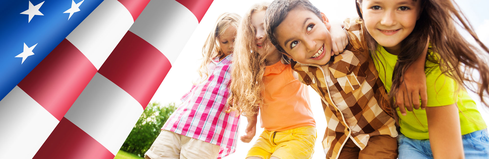 Three joyful young girls playing outdoors on synthetic grass, with a waving American flag in the background.