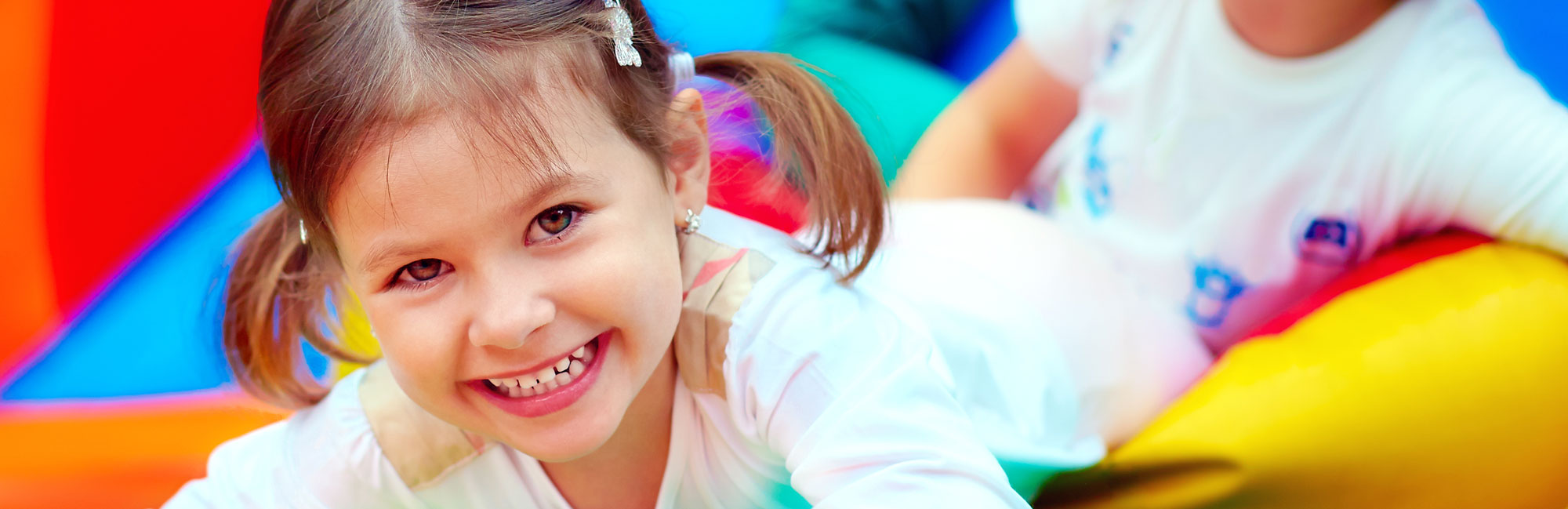 A cheerful young girl with pigtails smiling while playing on an inflatable bounce house.