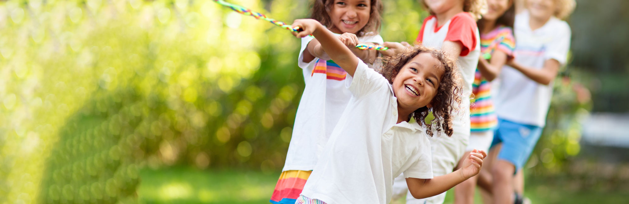 Young girls playing tug-of-war on a lush green field, laughing and enjoying the activity.