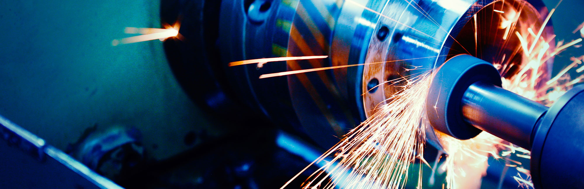 Industrial grinding process with sparks flying from a rotating metal part being machined.