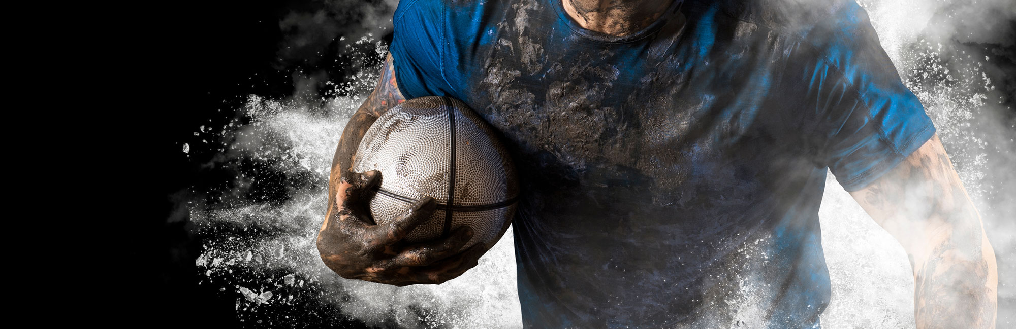 Athlete holding a muddy rugby ball, symbolizing strength and determination.