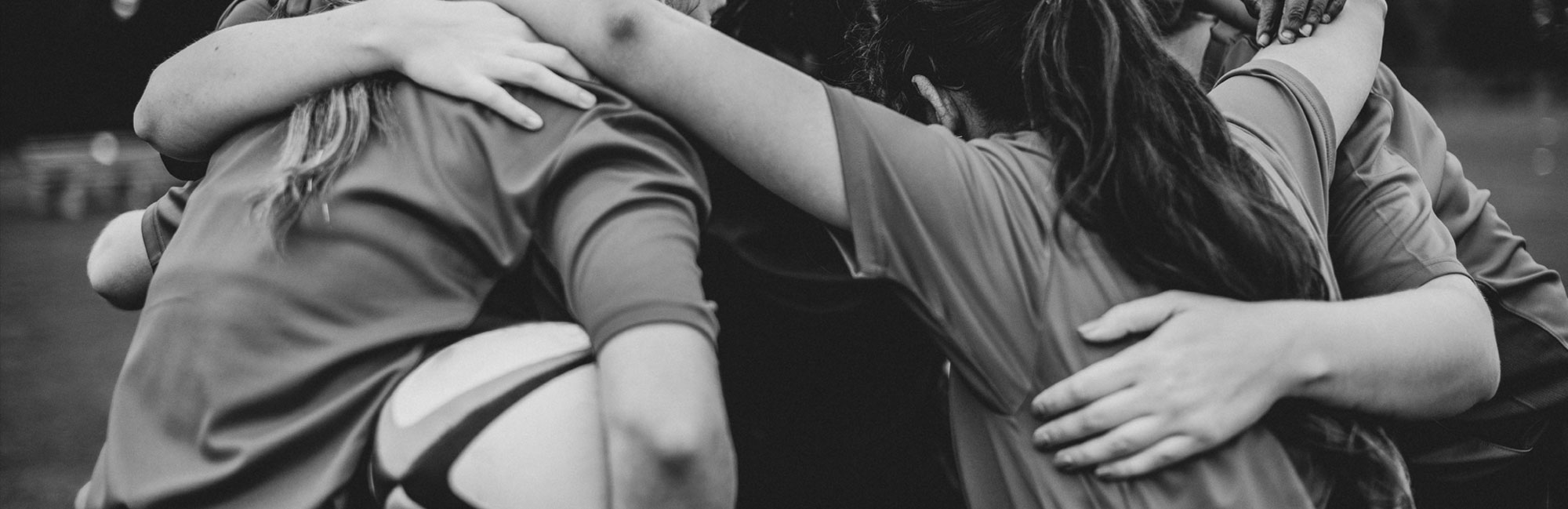 Black and white image of soccer players embracing in celebration after a goal.