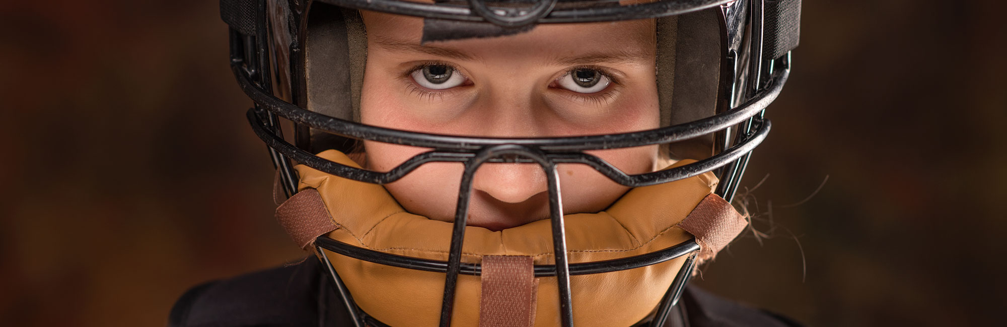 Close-up of a determined softball catcher wearing protective gear, including a helmet and padded glove, ready for the game.