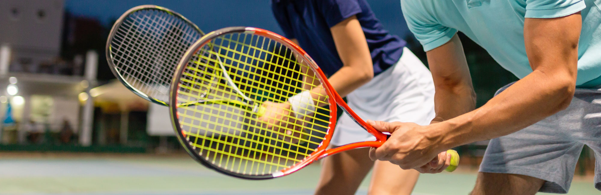 Two players engaged in a tennis doubles match, focusing on a ball in mid-air.