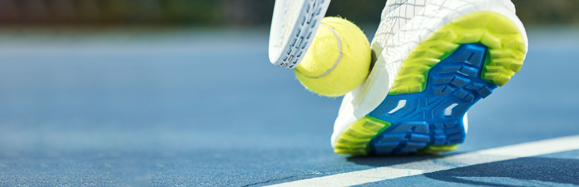 Tennis player in motion, stepping on the court with a ball bouncing nearby.