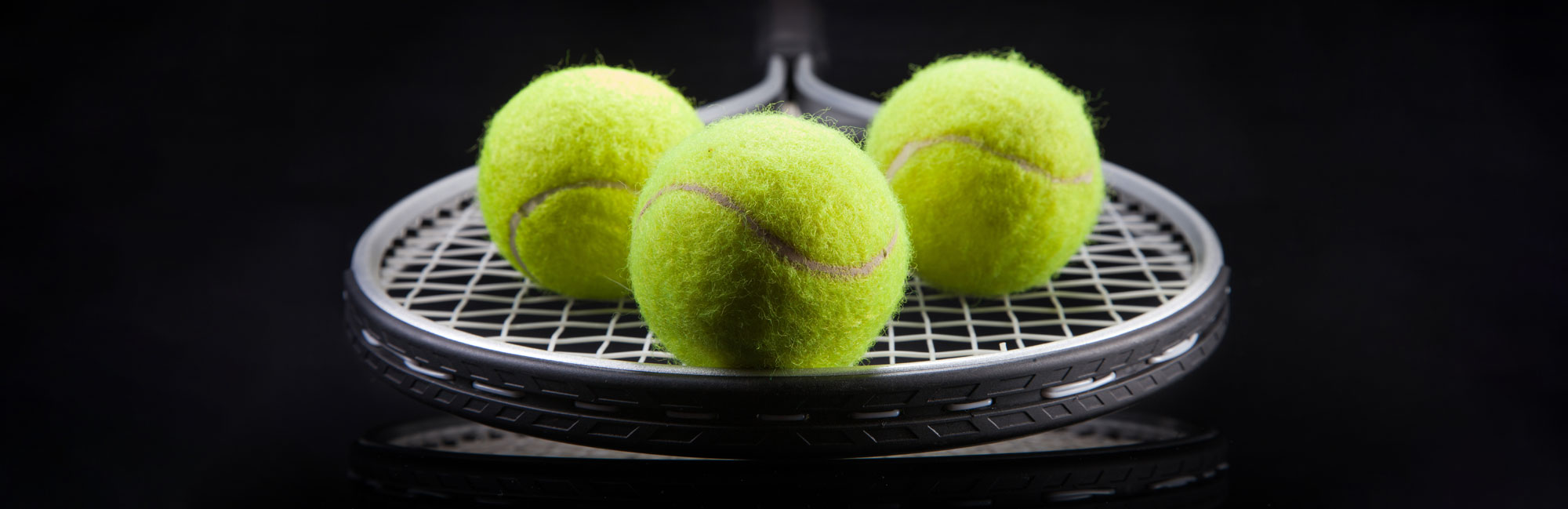 Three bright yellow tennis balls resting on a racket against a dark background.